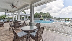 A covered outdoor area with wicker furniture, a pool, and a view of palm trees.