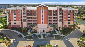 A multi-story hotel with a central entrance, multiple balconies, and a parking area with a curved road.