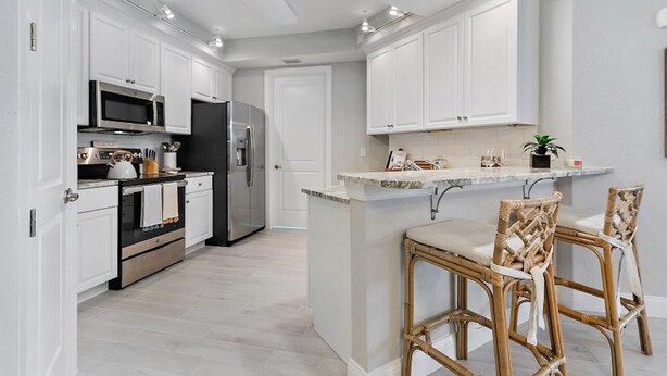 A modern kitchen with white cabinets, stainless steel appliances, and a central island with bar stools.