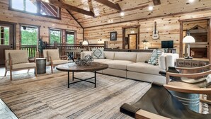 A cozy cabin interior with a wooden ceiling, a large sofa, a coffee table, and a dining area. - Giant Luxury 10BR Cabin Huge Outdoor Area, Pool (Sevierville)