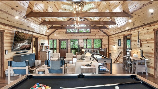 A wooden cabin interior with a pool table, seating area, and large windows. - Giant Luxury 10BR Cabin Huge Outdoor Area, Pool (Sevierville)