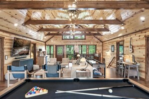 L’intérieur d’un chalet en bois comprend une table de billard, un coin salon et de grandes fenêtres.