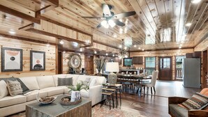 A spacious living room with a large sofa, coffee table, and a dining area with a table and chairs. - Giant Luxury 10BR Cabin Huge Outdoor Area, Pool (Sevierville)