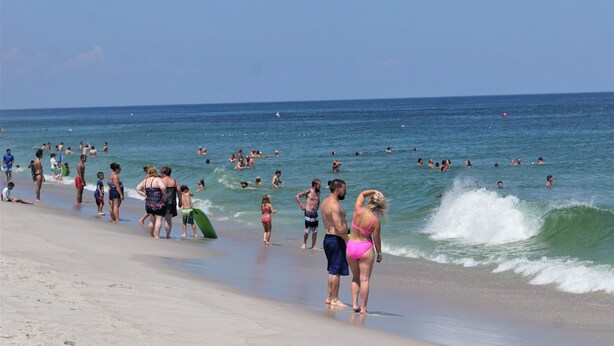 Een druk strand met mensen die wandelen en zwemmen.