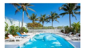 Une piscine entourée de chaises longues blanches et de palmiers.