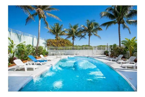 A swimming pool with white lounge chairs and palm trees.