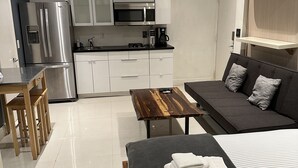Un espace de vie moderne et compact comprenant un coin cuisine, un espace repas et un canapé convertible.