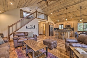 A spacious living area with a wooden ceiling, leather sofas, a wooden coffee table, and a kitchen in the background. - Rocky Mountain Alma Cabin with Deck & Hot Tub! (Alma)