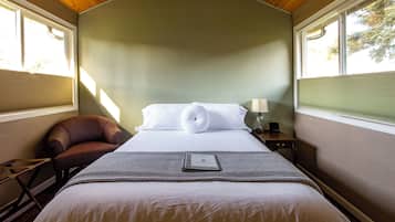 A neatly made bed with pillows and a book, a brown leather chair, and a nightstand with a lamp.