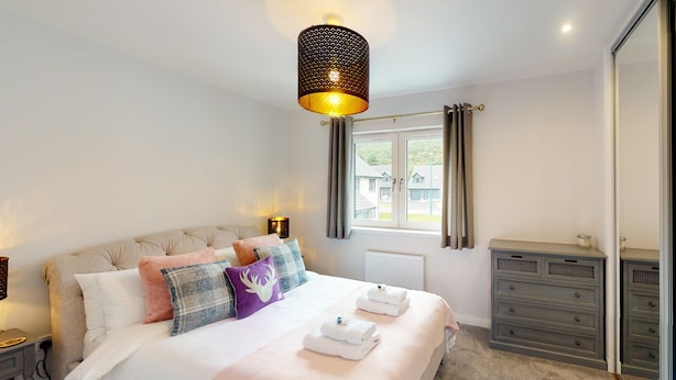 Quarto bem arrumado com uma cama grande, mesas de cabeceira, cômoda e uma janela com cortinas.