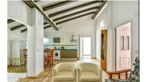 Ampla sala de estar com cozinha ao fundo, área de refeições com cadeiras e uma porta que dá para outro cômodo.