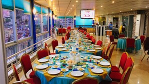 A banquet hall with round tables set for a meal, red chairs, and a large screen displaying an image. - Konerkon Otel Plaza (Ermenek)