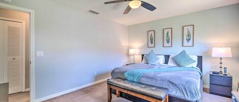 Un dormitorio con cama, mesitas de noche, un banco, ventilador de techo y cuadros en la pared.