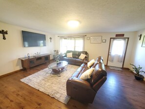 A living room with a leather sofa, a glass coffee table, a TV, and a wooden floor.