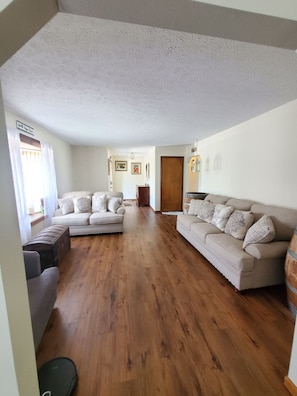 Un salon spacieux avec deux canapés, un plancher en bois et une porte donnant sur une autre pièce.