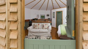 Un intérieur chaleureux avec un plafond en bois, un canapé blanc agrémenté de coussins à motifs floraux et un coin cuisine doté de meubles et d’un plan de travail en bois.