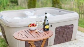 Un bain à remous avec une table en bois devant, une bouteille de vin et un saladier de fraises.