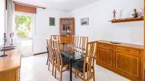 Un coin repas comprenant une table à plateau en verre, des chaises en bois, un meuble et une étagère ornée d’objets décoratifs.