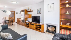 Un salon équipé d’un téléviseur, d’un meuble de rangement en bois, d’une cheminée et d’un coin repas avec des chaises et une table.