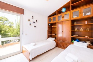 A hotel room with two beds, a large wooden wardrobe, and a balcony with a view of greenery.
