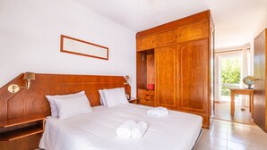 Une chambre d’hôtel avec un grand lit, une armoire en bois et une petite table avec une lampe.
