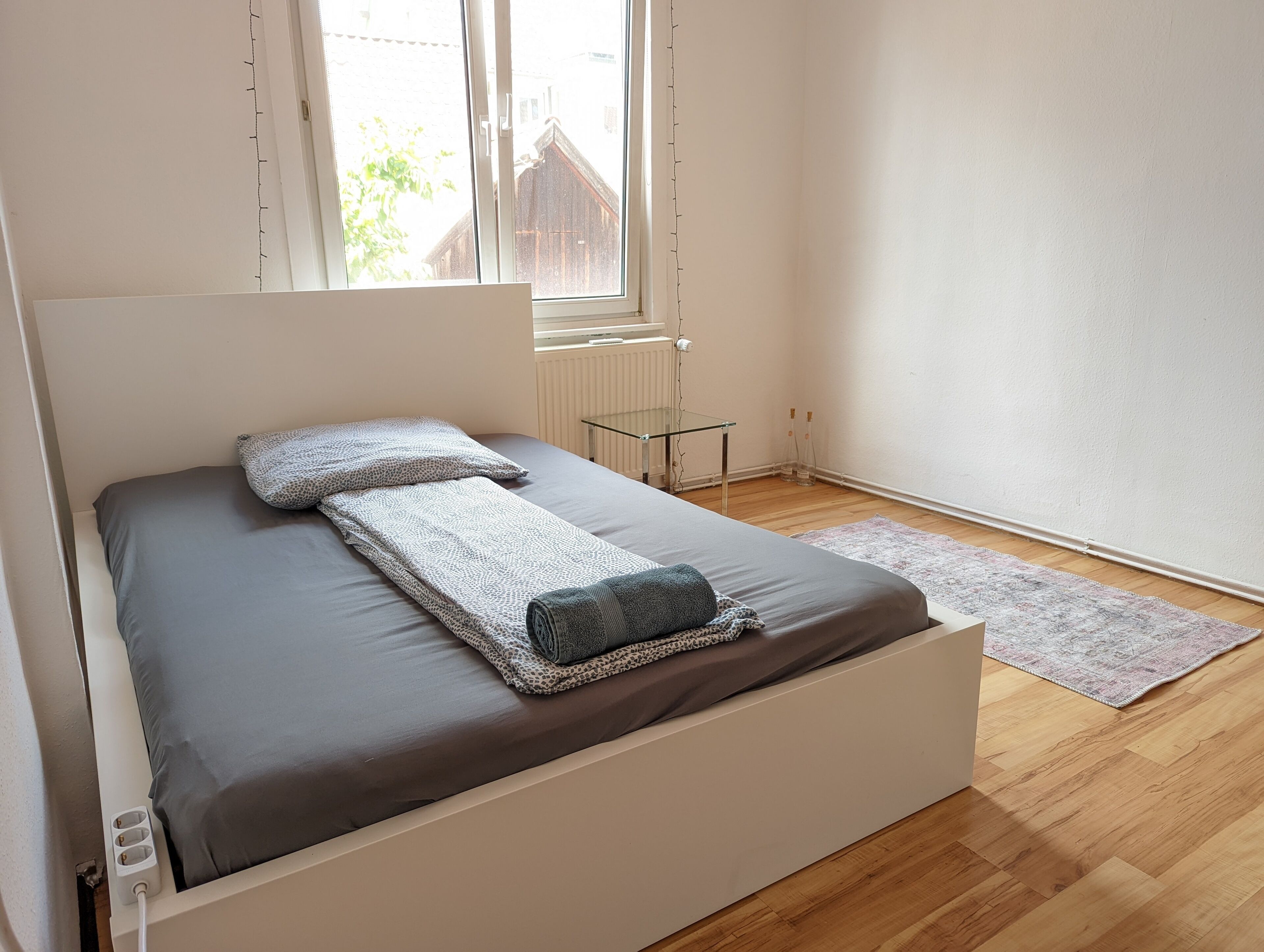 Et moderne soveværelse med en seng, et glasnatbord, en radiator og udsigt ud