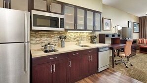 A modern kitchen with stainless steel appliances, dark wood cabinets, a tiled backsplash, and a dining area with a desk and chair. - Queen Studio Suite w/ Kitchen Near Disney (Anaheim)