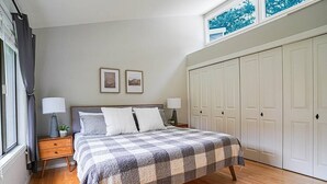 Une chambre à coucher avec une couvre-lit à carreaux, deux lampes de chevet, une table de chevet, une fenêtre avec des rideaux et une armoire.