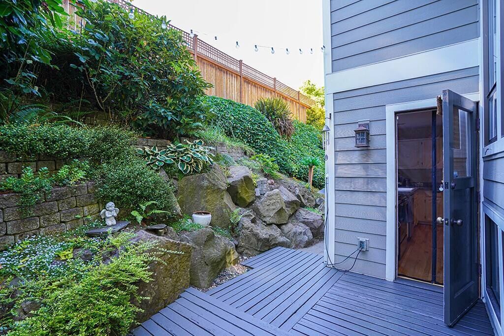 A deck with a stone wall and greenery, a wooden fence, and a building entrance.