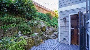 Une terrasse avec un mur en pierre et de la verdure, une clôture en bois et l’entrée d’un bâtiment.