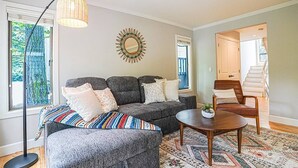 Un salon avec un canapé d’angle gris, une table basse ronde et un tapis à motifs.