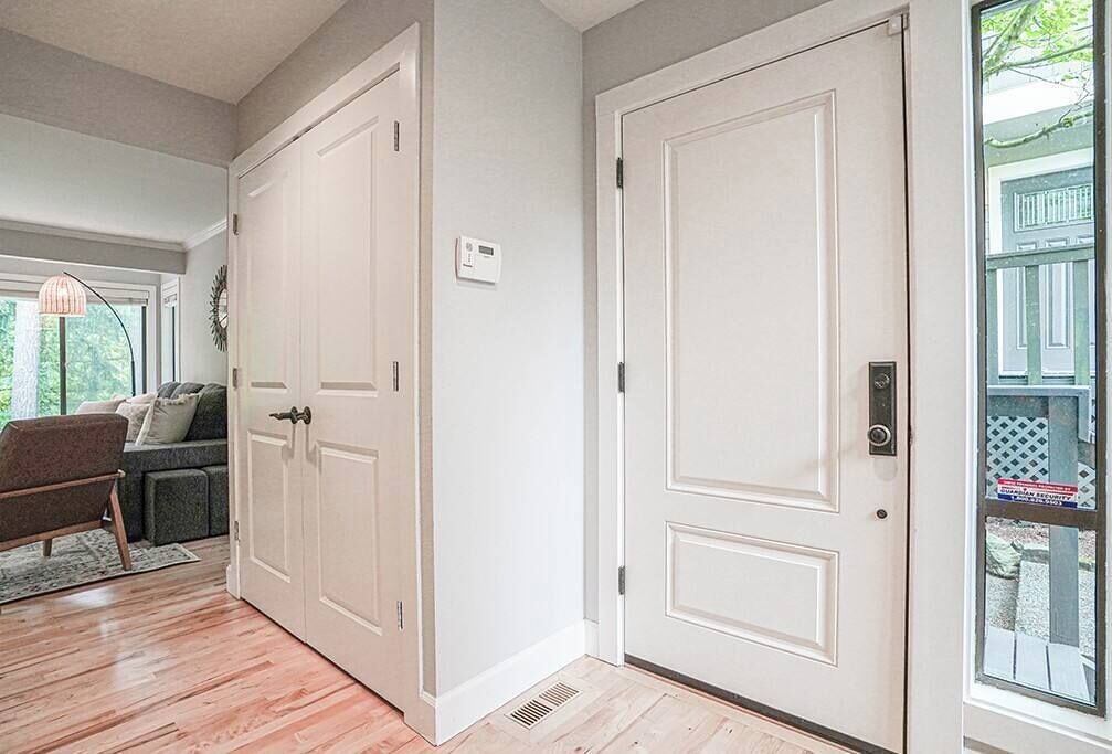 A hallway with a white door, a thermostat, and a window with a view of greenery.
