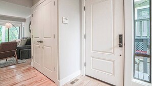 Un couloir avec une porte blanche, un thermostat et une fenêtre donnant sur un paysage verdoyant.