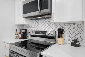 A modern kitchen with stainless steel appliances, white cabinetry, and a patterned backsplash. - SoDo Love 2 (Orlando)
