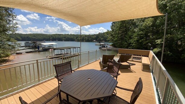 A deck with a table and chairs, overlooking a lake with boats and docked at a pier. - Beautiful Lake Lanier Home, 2 story dock, Paddle Boards, & Pedle Boat (Dawsonville)