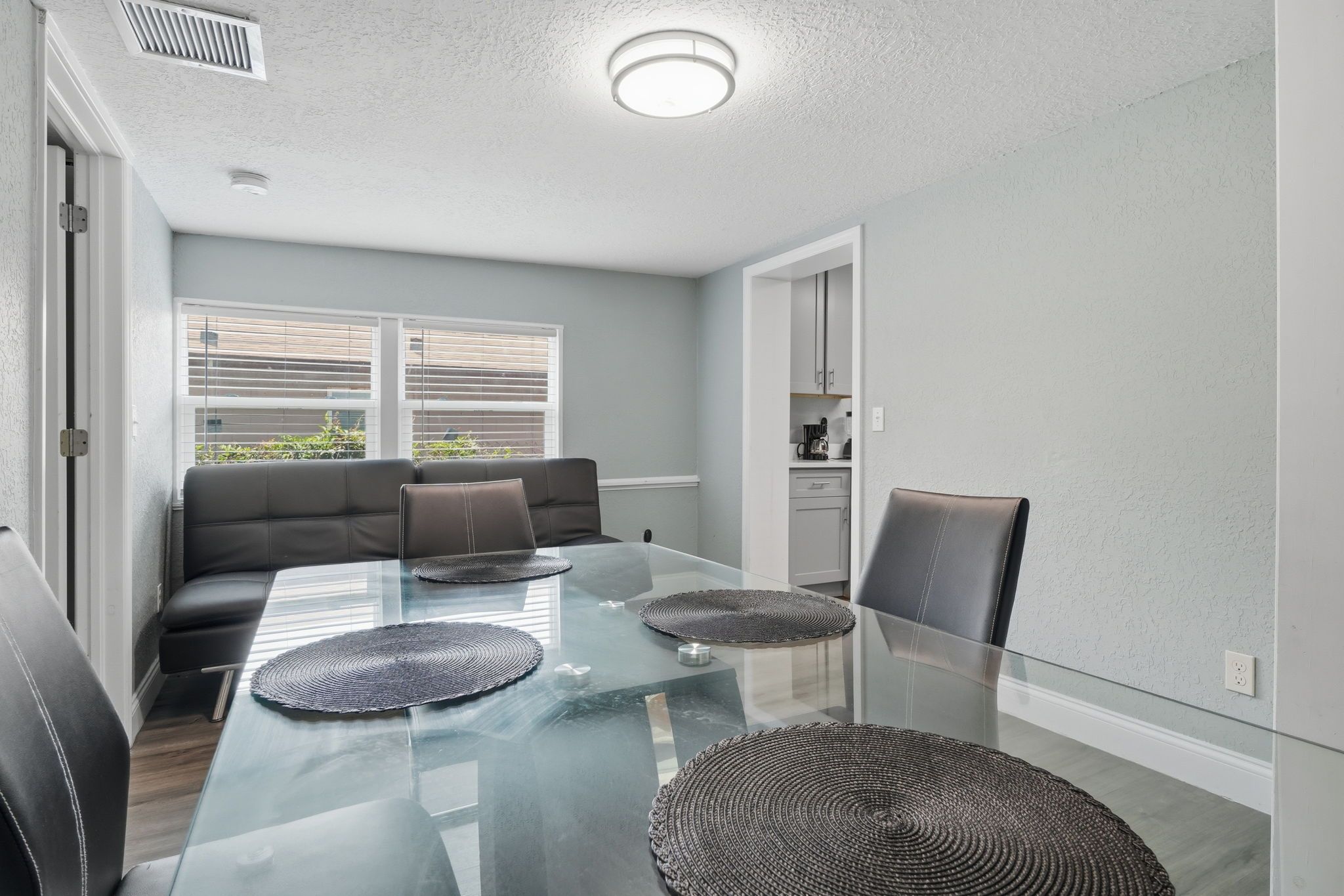 A modern dining area with a glass table, black leather chairs, and a grey sofa.