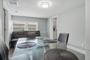 A modern dining area with a glass table, black leather chairs, and a grey sofa.