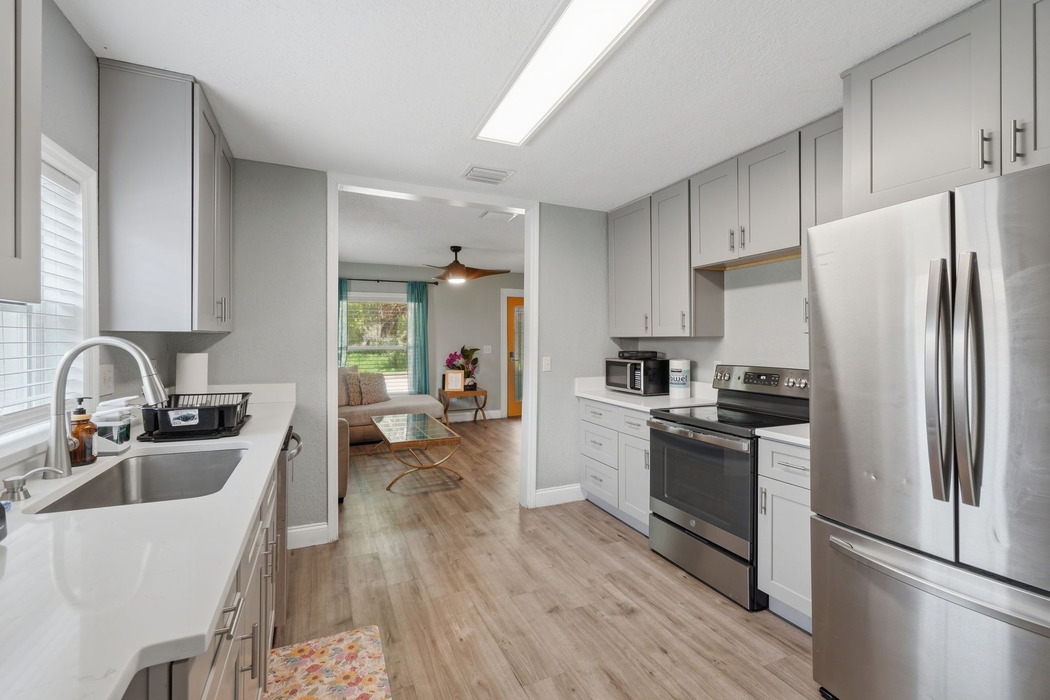 A modern kitchen with stainless steel appliances, a dining area with a sofa and table, and a view of the outdoors.