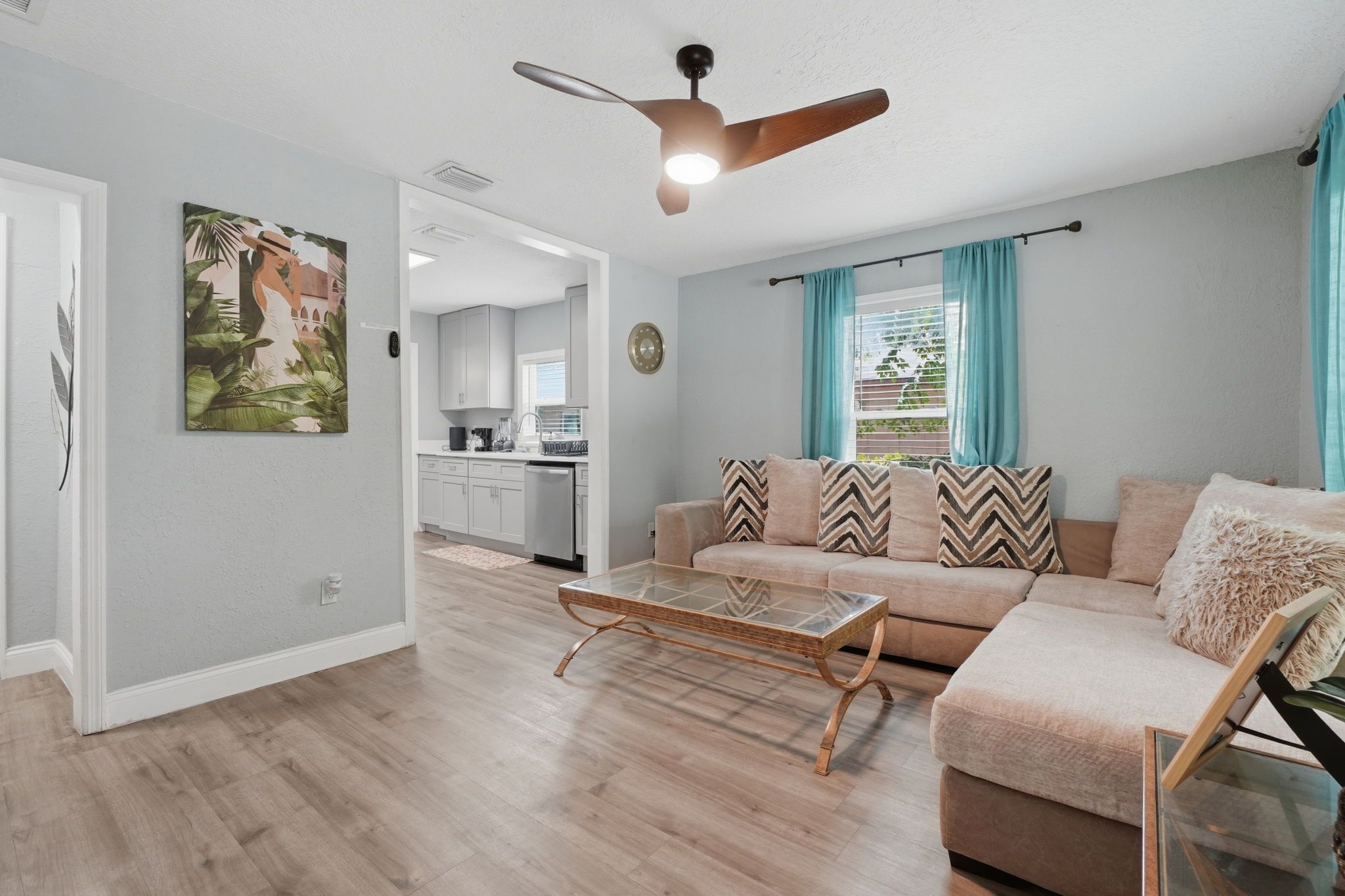 A modern living room with a sofa, a glass coffee table, and a ceiling fan.