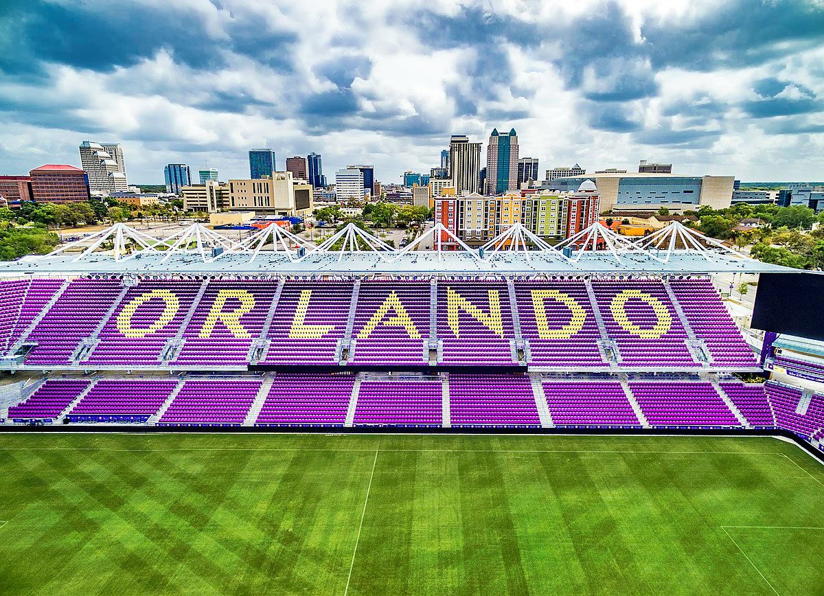Un estadio con la palabra 'ORLANDO' escrita en los asientos, rodeado por un paisaje urbano.