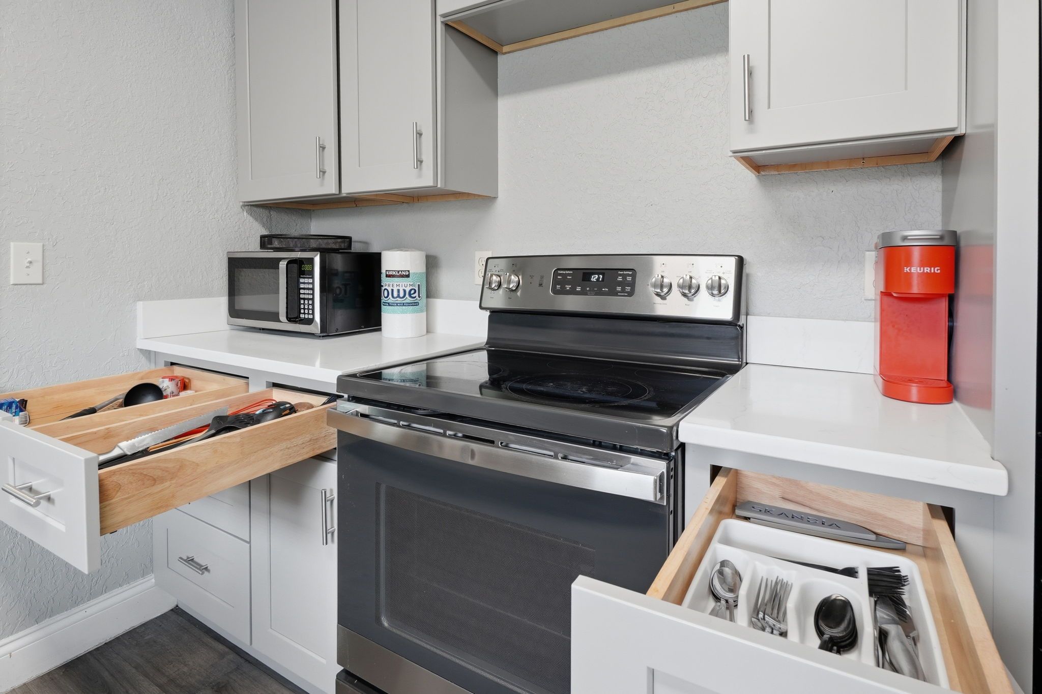 A compact kitchen with white cabinets, a microwave, an oven, and a coffee maker.