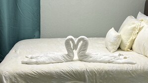 Een bed met een witte dekbedovertrek en kussens, een blauwgroene gordijn en een handdoek in de vorm van een hart.