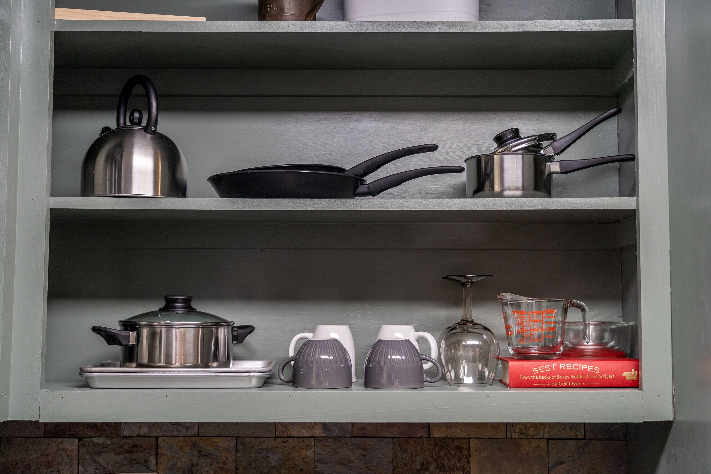 A kitchen shelf with various cookware and a cookbook.
