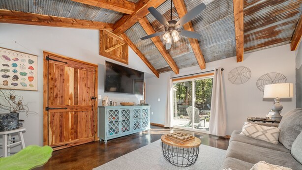 A spacious living room with a wooden ceiling, a large TV, a dining area with a blue cabinet, and a view through a glass door. - Romantic Waterfall cabin-Hot Tub-Coffee & Tea Bar-Fire Pit (Hot Springs)