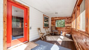A wooden cabin with a red door, two windows, a wooden table, and two chairs. - Romantic Waterfall cabin-Hot Tub-Coffee & Tea Bar-Fire Pit (Hot Springs)
