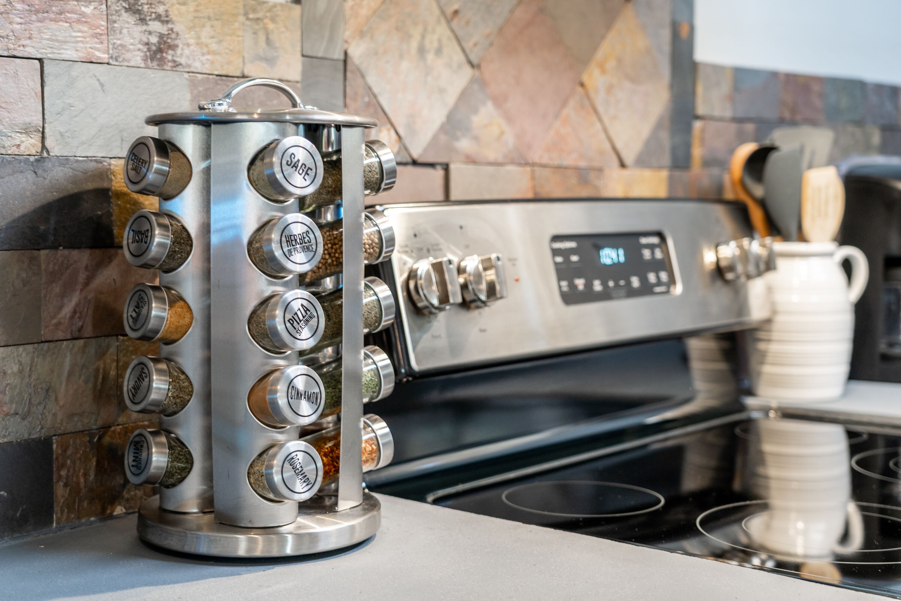 Una cafetera de acero inoxidable con varias opciones de preparación, una cocina moderna con salpicadero de piedra y una taza blanca sobre la encimera.