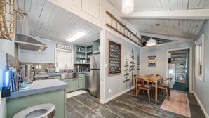 A kitchen with a wooden ceiling, a dining area with a table and chairs, and a chalkboard wall with writing. - Romantic Waterfall cabin-Hot Tub-Coffee & Tea Bar-Fire Pit (Hot Springs)