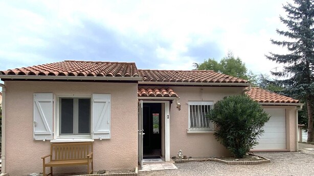 Una casa de dos pisos con techo de tejas, camino de grava y un pequeño banco de madera.