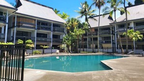 A hotel with a swimming pool surrounded by palm trees and a clear blue sky. - Polynesian Koi Pond Gardens Condo in Hilo w pool (Hilo)