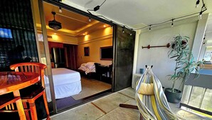 A hotel room with a bed, a desk, a chair, a hammock, and a potted plant. - Polynesian Koi Pond Gardens Condo in Hilo w pool (Hilo)